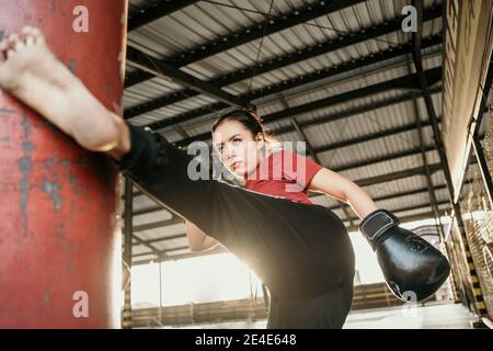 Die junge Frau trainiert einen Kick auf den Boxsack Im Fitnessstudio Stockfoto