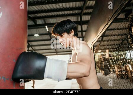 asiatische Mann Boxer Prüfung Übung schlagen Boxsack beim Training Lager Stockfoto