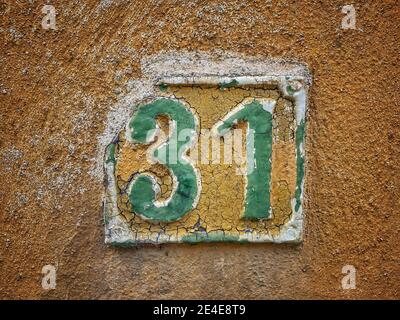 Nummer 31, die Anzahl der Häuser, Wohnungen, Straßen. Die grüne Zahl auf der gelben Metallplatte, die Hausnummer einunddreißig (31) auf der rauen Wand. Stockfoto