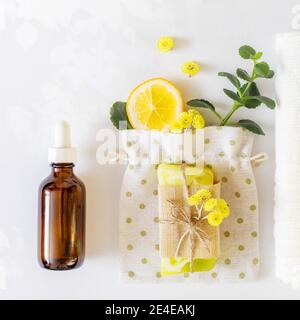 Ein Stück handgemachte Naturseife oder Trockenshampoo mit Blumen, Handtüchern und einer Flasche Öl. Handhygiene. Nahaufnahme von Wellness-Produkten aus der Natur Stockfoto