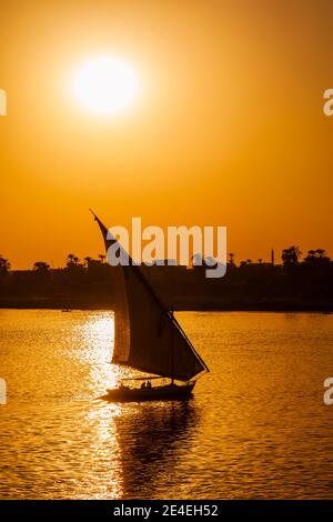 Eine typische Felucca, die auf dem Nil nahe Luxor segelt, Ägypten, das gegen die untergehende Sonne am Sonnenuntergang silhouetted Stockfoto