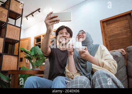 Glücklich junge asiatische Paar unter Selfies mit einem Smartphone Kamera beim Witzeln und Kaffee im Wohnzimmer genießen Stockfoto