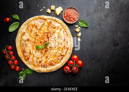 Leckere Pizza mit Huhn und Süße und saure Sauce und Zutaten für die Küche Tomaten und Basilikum auf schwarzem Hintergrund. Draufsicht Stockfoto