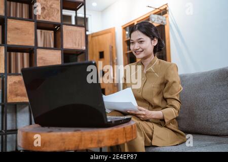 Frau in Regierungsuniform hält Papiere, während sie von zu Hause aus arbeitet Online über Laptop-Computer Stockfoto