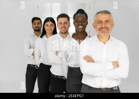 Porträt einer lächelnden Gruppe von verschiedenen Unternehmenskollegen in weißen Hemden stehend in einer Reihe zusammen in einem hellen modernen Büro, lächelnd und aussehend Stockfoto