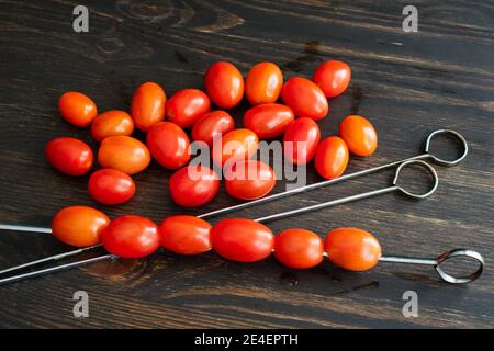 Threading Grape Tomatoes onto Metal Skewers: Making grape tomato kebabs for the grill Stockfoto