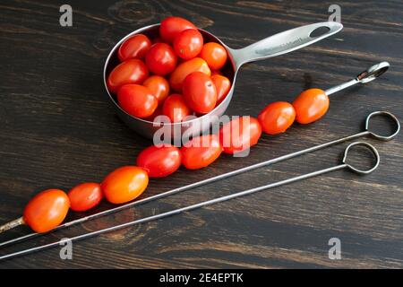 Threading Grape Tomatoes onto Metal Skewers: Making grape tomato kebabs for the grill Stockfoto