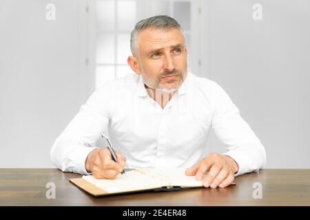 Reifer bärtiger Geschäftsmann, der an der Rezeption im Büro schreibt. Er arbeitet hart, von zu Hause oder im Büro Stockfoto