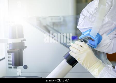 Laborwissenschaftler tragen Schutzkleidung auf der Suche nach Mikroskopen, während sie medizinische Forschung in einem Labor betreiben. Stockfoto