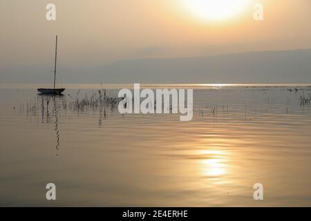 Boot schwimmt auf dem ruhigen Wasser unter herrlichem Sonnenuntergang. Sonnenaufgang über dem See. Stockfoto