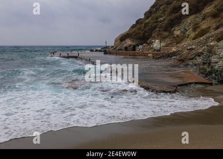 Agkali Beach, Folegandros Island, Griechenland - 24. September 2020: Ein Betonkai an einem Sandstrand, überflutet von den Wellen des rauen Meeres. Stockfoto