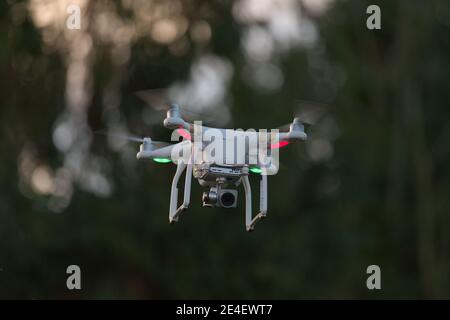 Fliegende Quad Copter UAV Drohne schwebend mit unfokussierter Baum Hintergrund. Aufgenommen während der goldenen Stunde am Abend bei Sonnenuntergang. Stockfoto