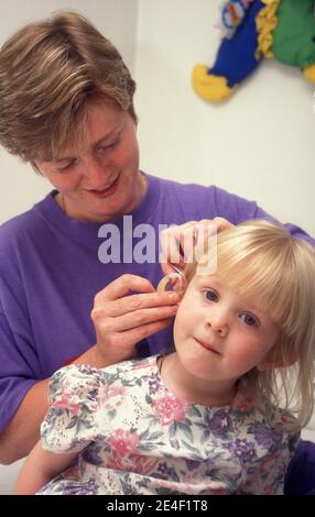Frau, die ein Hörgerät in das Ohr eines tauben Kindes einführt Stockfoto