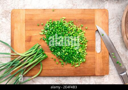 Gehackter Bund von grünem Knoblauch auf Holz Schneidebrett mit Messer. Kochen. Lebensmittelzutat. Flta Lay Stockfoto