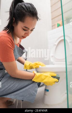 Frau mit einem Gummihandschuh reinigt eine Toilettenschüssel in Das Badezimmer Stockfoto