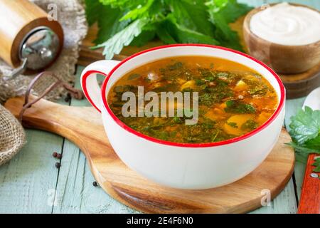 Frische hausgemachte Brennnessel- und Fleischsuppe mit Sauerrahm auf einem rustikalen Tisch. Speicherplatz kopieren. Stockfoto