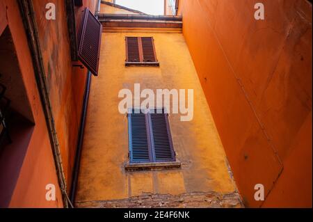 Italienische Fenster an der orangefarbenen Wandfassade mit geschlossenem Braun Farbe schuppige klassische Fensterläden Stockfoto