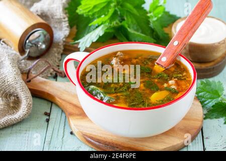 Frische hausgemachte Brennnessel- und Fleischsuppe mit Sauerrahm auf einem rustikalen Tisch. Stockfoto