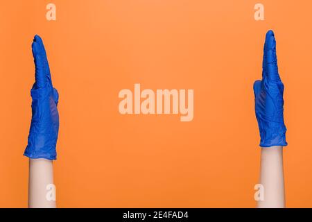 Männliche Hände in medizinischen schützenden Latexhandschuhen zeigen große Geste, zeigen etwas weit, isoliert auf orangenen Studio-Hintergrund Stockfoto