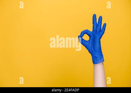 Nahaufnahme der männlichen Hand in medizinischen Schutzhandschuhen zeigt ok Zeichen, isoliert in gelben Studio-Hintergrund mit Kopierraum Stockfoto