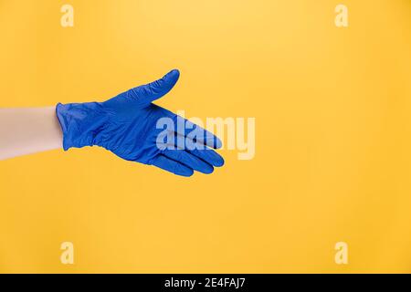 Willkommensgeste. Offene Handfläche. Nahaufnahme der nicht erkennbaren männlichen Hand in blauen Schutzhandschuhen, isoliert auf gelbem Hintergrund mit Kopierraum Stockfoto