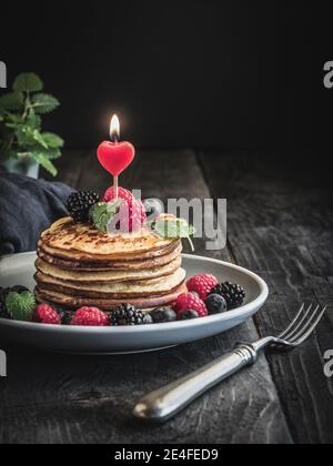 Pfannkuchen mit frischen Beeren, Minze und Kerze mit Herzform auf dem Teller und Holz Vintage-Tisch. Speicherplatz kopieren. Stockfoto