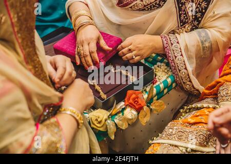 Ältere Frauen öffnen Samtboxen mit goldenen Schmuckohrringen Für indische Braut während der Hochzeit Henna mehndi sangeet Party-Nacht Stockfoto