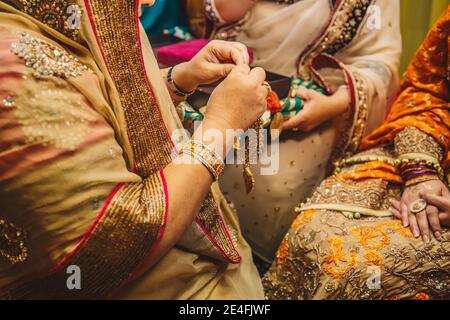 Schwiegermutter Hände gehen zu goldenen Schmuck Halskette tragen Auf Braut während Henna mehndi sangeet indisch pakistanischen weiblichen Partei Nacht Stockfoto