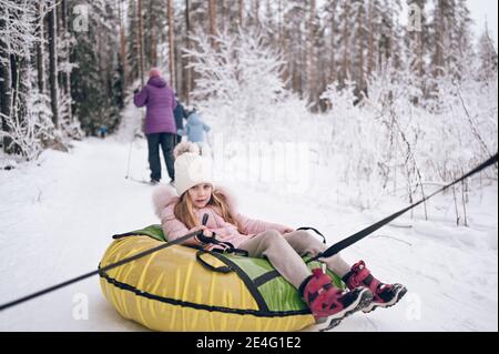 Kleine niedliche Mädchen in rosa warm outwear mit Spaß Fahrten aufblasbare Schneeröhre in schneeweißen kalten Winter im Freien. Familien Sport Urlaub Aktivitäten Stockfoto