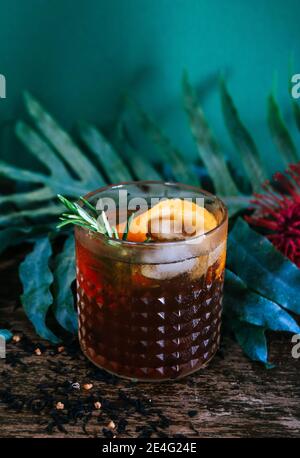 Altmodischer Rum oder Whiskey-Cocktail vor einem botanischen, tropischen, dunkelgrünen Hintergrund Stockfoto