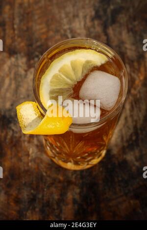 Eistee in einem Cocktailglas auf einem Holz stehend Tisch vor einer weißen Wand draußen mit Schatten Von einer Palmenblattpflanze im Hintergrund Stockfoto