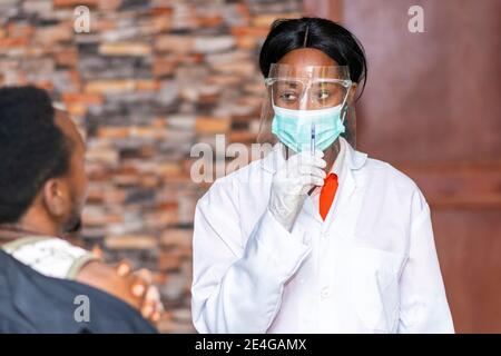 Medizinisches Personal trägt Gesichtsmaske und Gesichtsschutz und hält Eine Spritze, die einen Patienten ansieht Stockfoto