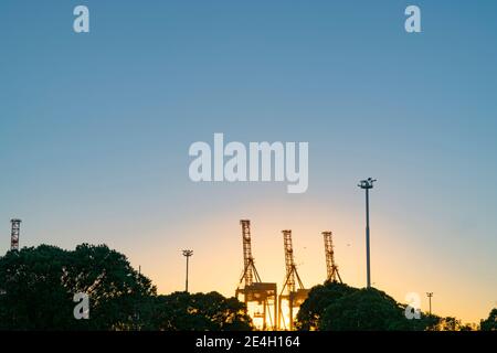 Containerkrane am Hafen von Tauranga Anlage durch aufgehende Sonne am Sulphur Point in der Stadt hinterleuchtet. Stockfoto