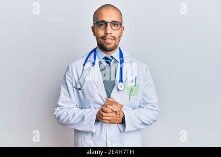 Hispanic erwachsenen Mann trägt Arzt Uniform und Stethoskop mit Händen zusammen und gekreuzte Daumen lächelnd entspannt und fröhlich. Erfolg und optimistisch Stockfoto