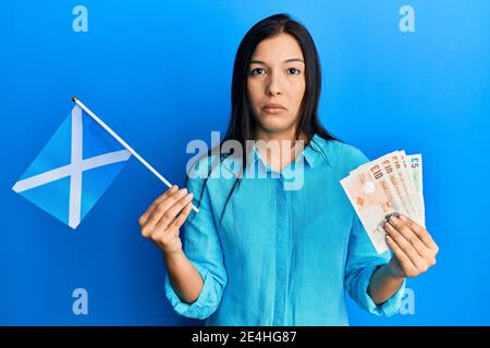 Junge lateinerin hält schottland Flagge und Pfund Banknoten entspannt mit ernster Ausdruck auf Gesicht. Einfach und natürlich Blick auf die Kamera. Stockfoto