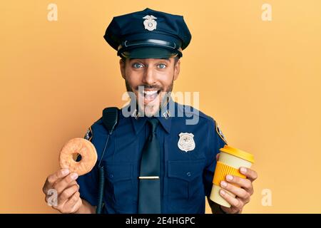 Schöner hispanischer Polizeimann, der Donut isst und Kaffee trinkt, lächelt und lacht laut, weil lustig verrückter Witz. Stockfoto