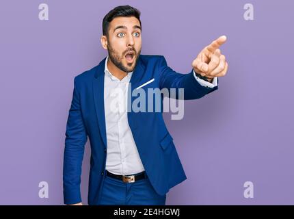 Junger hispanischer Mann trägt Business Jacke zeigt mit Finger überrascht voraus, offenen Mund erstaunt Ausdruck, etwas auf der Vorderseite Stockfoto