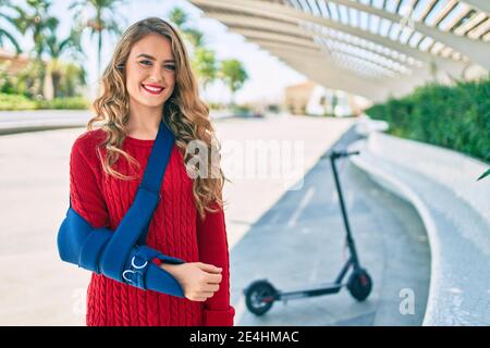 Junge blonde Mädchen lächelnd glücklich verletzt mit Arm Sling stehen im Park. Stockfoto