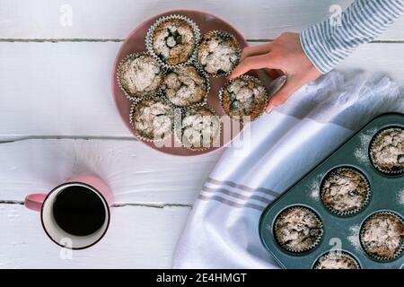 Die Hand des Mädchens nimmt den Muffin vom Teller, Draufsicht, flach liegend. Stockfoto