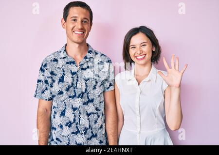 Schönes Paar trägt legere Kleidung zeigt und zeigt mit den Fingern Nummer fünf, während lächelnd zuversichtlich und glücklich. Stockfoto