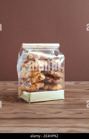 Shortbread-Kekse mit Mandelflocken in transparentem Beutel auf einem Holztisch gegen braune Wand. Nahaufnahme Stockfoto