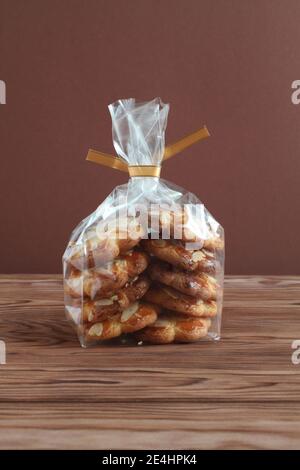 Shortbread-Kekse mit Mandelflocken in transparentem Beutel auf einem Holztisch gegen braune Wand. Nahaufnahme Stockfoto