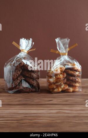 Schokoladen-Haferflocken-Kekse und Shortbread-Kekse mit Mandelflocken in transparenten Tüten auf einem Holztisch. Nahaufnahme Stockfoto