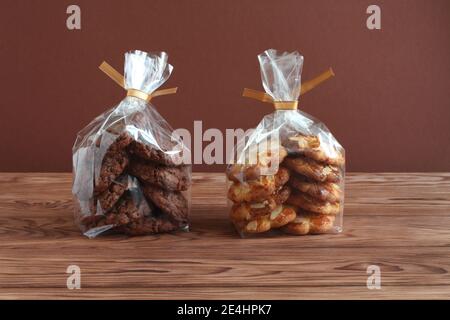 Schokoladen-Haferflocken-Kekse und Shortbread-Kekse mit Mandelflocken in transparenten Tüten auf einem Holztisch. Nahaufnahme Stockfoto