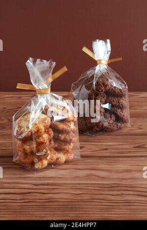 Schokoladen-Haferflocken-Kekse und Shortbread-Kekse mit Mandelflocken in transparenten Tüten auf einem Holztisch. Nahaufnahme Stockfoto