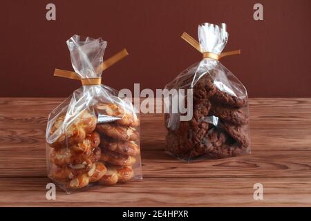 Schokoladen-Haferflocken-Kekse und Shortbread-Kekse mit Mandelflocken in transparenten Tüten auf einem Holztisch. Nahaufnahme Stockfoto