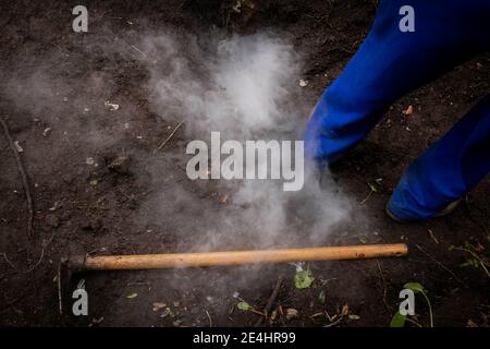 Hacke auf dem Boden neben Rauch einer Holzkohle Brennofen Stockfoto