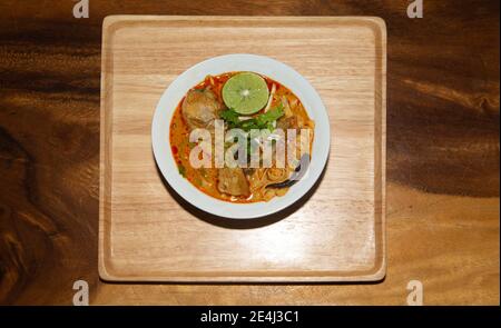 Draufsicht ein nordthailändisches Essen (Khao Soi), Rezept Curry Nudeln Suppe mit Huhn in einer Schüssel auf Holz Hintergrund. Stockfoto
