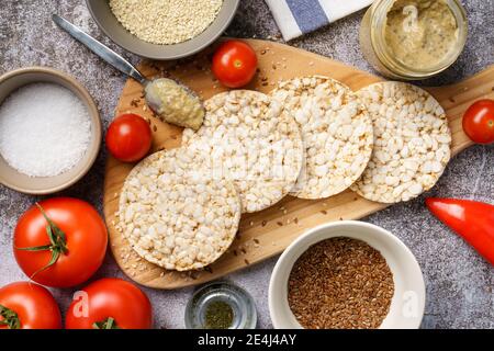 Knusprige Reiskuchen auf dem Tisch Hummus Aufstrich und Tomate Gemüse und Sesam auf dem Tisch - Draufsicht Auf gesundes vegetarisches oder veganes Frühstück Stockfoto