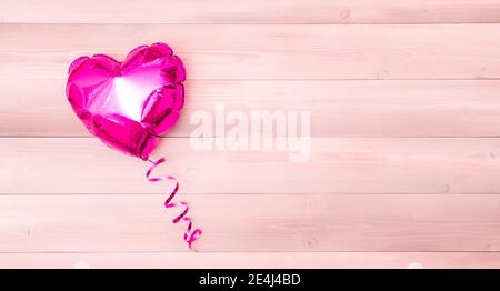 Ein rosa Folienballon in Herzform mit einem rosa Band auf einem beigen und rosa Holzhintergrund. Valentinstag. Das Konzept vom 14. Februar. Banner mit Copyspace. Platz für Text. Flatlay Stockfoto